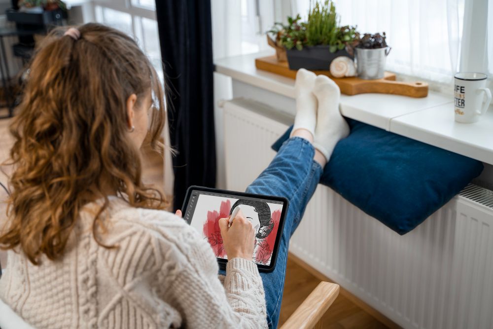 donna con i piedi appoggiati al radiatore elettrico con in mano un tablet